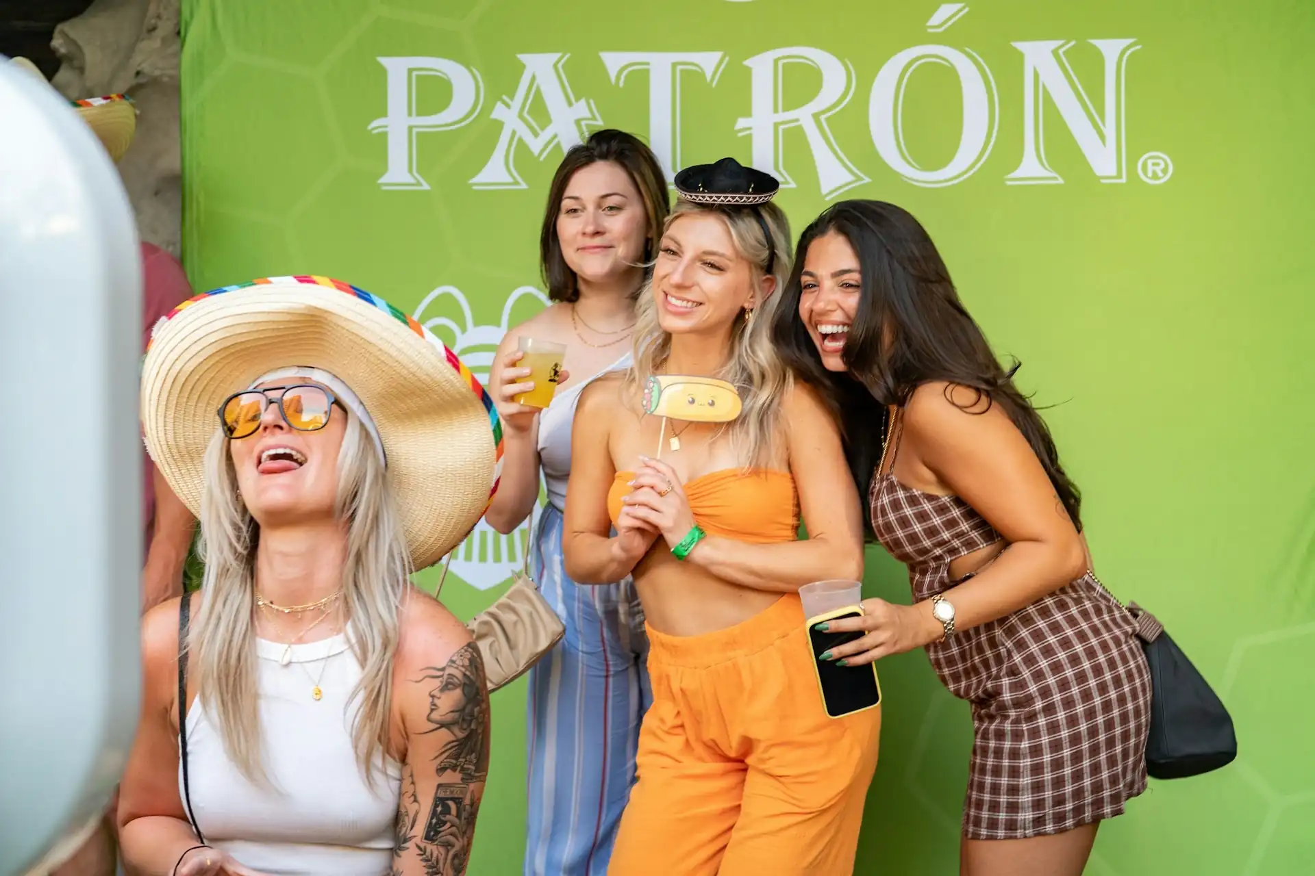 Friends laughing with props in front of a branded photo booth backdrop